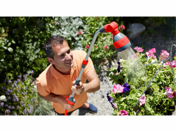 Un hombre con camisa naranja utiliza la bomba de bidón sin cable SHARE20V, sin batería ni cargador, para regar flores rosas y moradas.