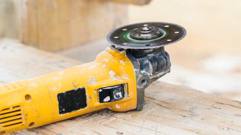 Yellow angle grinder with a circular blade on wood.