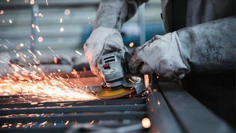 A person uses an angle grinder on metal, creating sparks and wearing protective gloves.