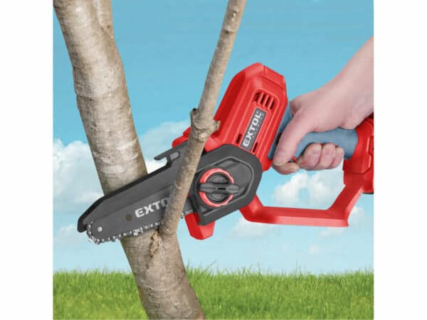 Someone prunes a tree branch with a red and black handheld chain saw in a grassy area under a blue sky.