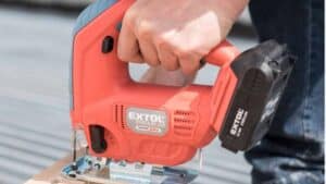 Someone cuts wood with a red Extol Premium cordless jigsaw.