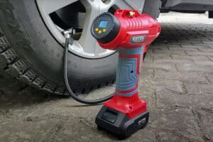 A digital tire inflator shows the pressure on its screen as it connects to a car tire beside the wheel on a paved surface.