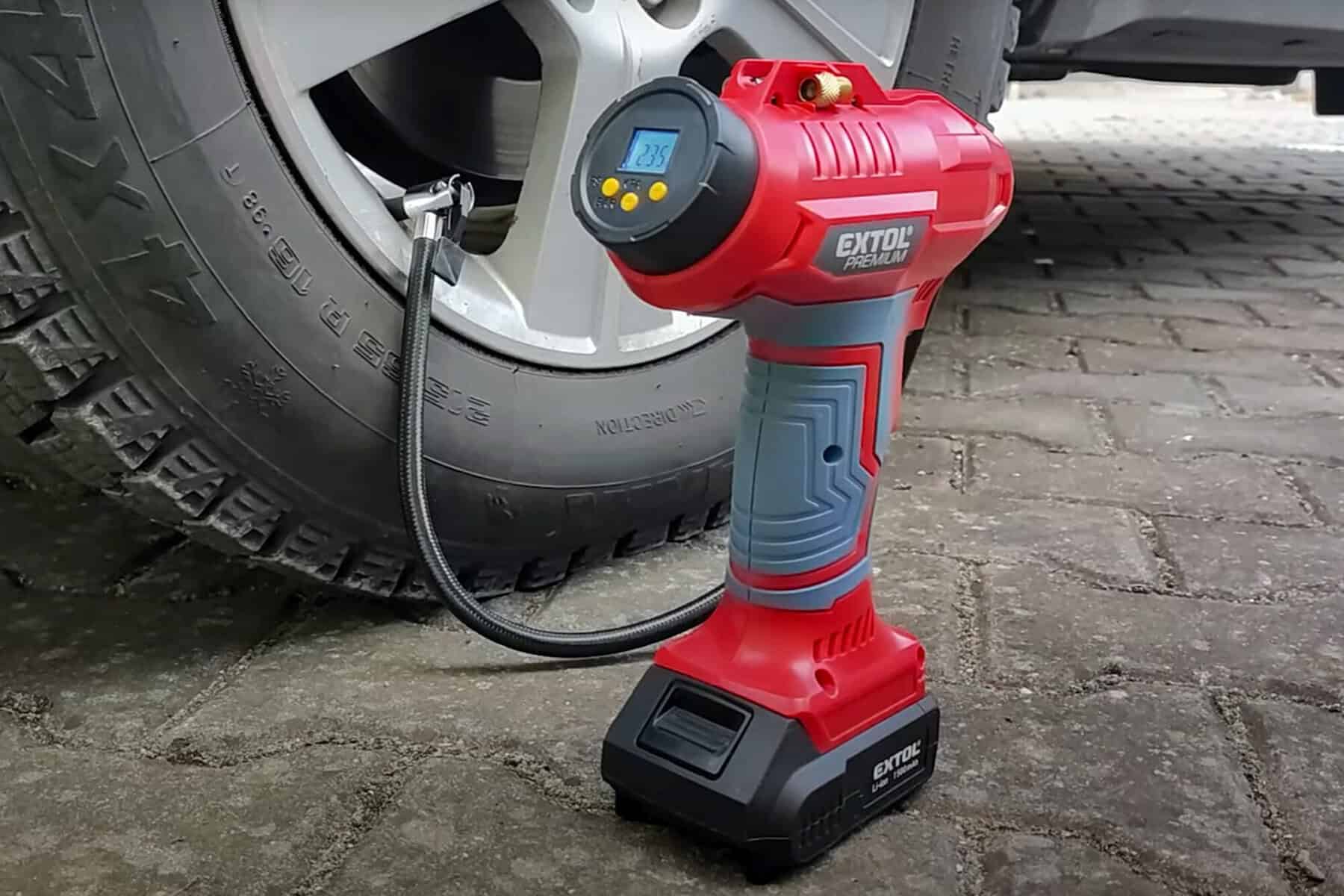 A digital tire inflator shows the pressure on its screen as it connects to a car tire beside the wheel on a paved surface.