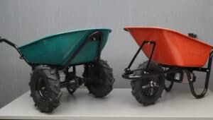 Green and orange wheelbarrows with rugged black wheels sit side by side on a white surface, gray background.
