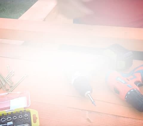 A blurry photo shows a workbench with screws, a drill, a yellow bit case, and someone in a red shirt.