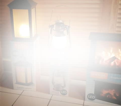 Three LED lanterns and boxes indoors, with one lantern lit brightly and overexposing the center of the photo.