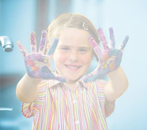 Smiling child indoors, wearing a striped shirt, holding up painted hands.