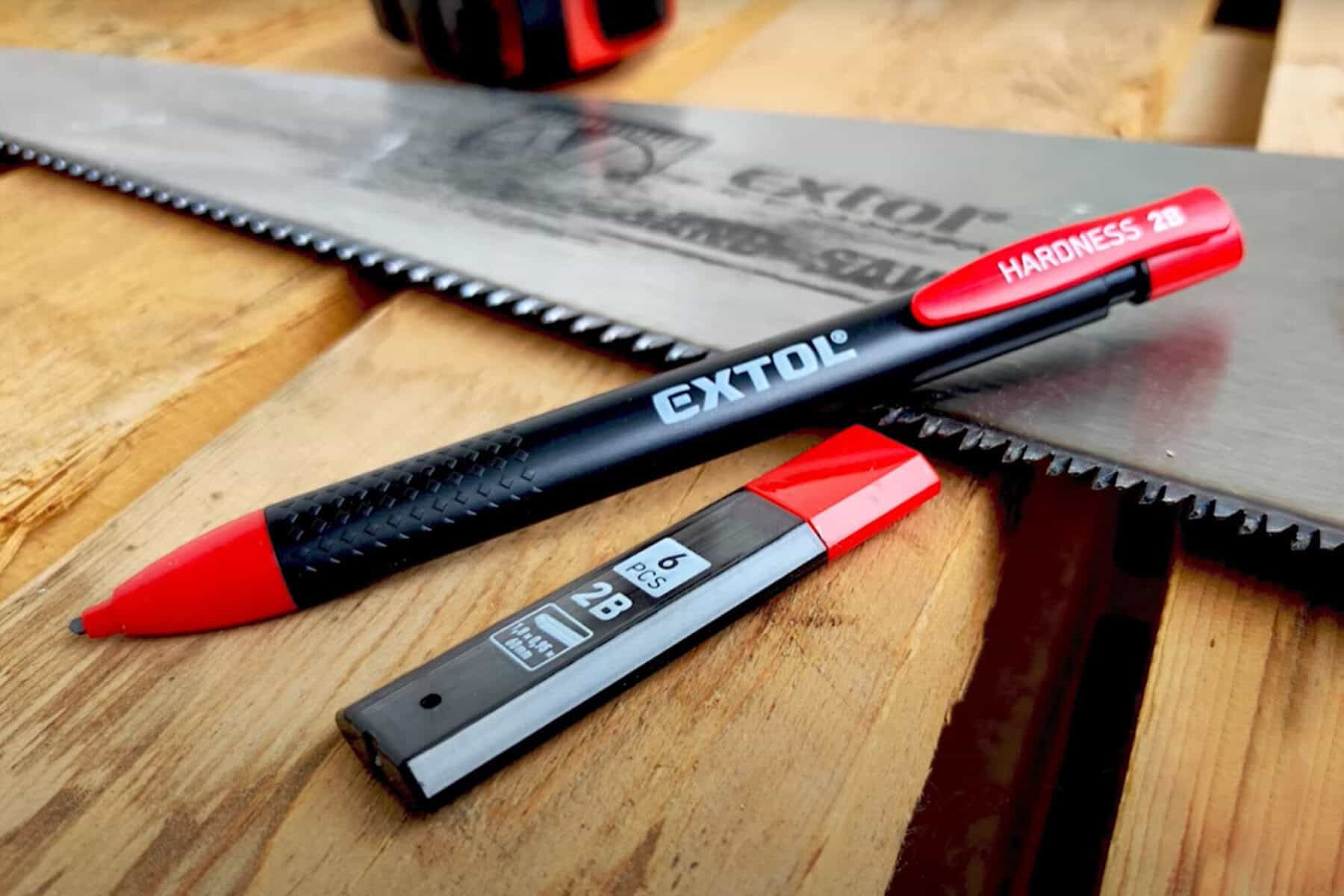 A "Hardness 2B" mechanical pencil and lead case lie on wood beside a toothed hand saw.