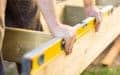 Someone checks a wooden beam's alignment with a yellow spirit level during construction.