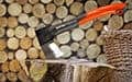 An orange-handled axe is stuck in a log, with stacked firewood behind it.
