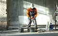 A construction worker in safety gear works with tools next to two buckets at a building site.