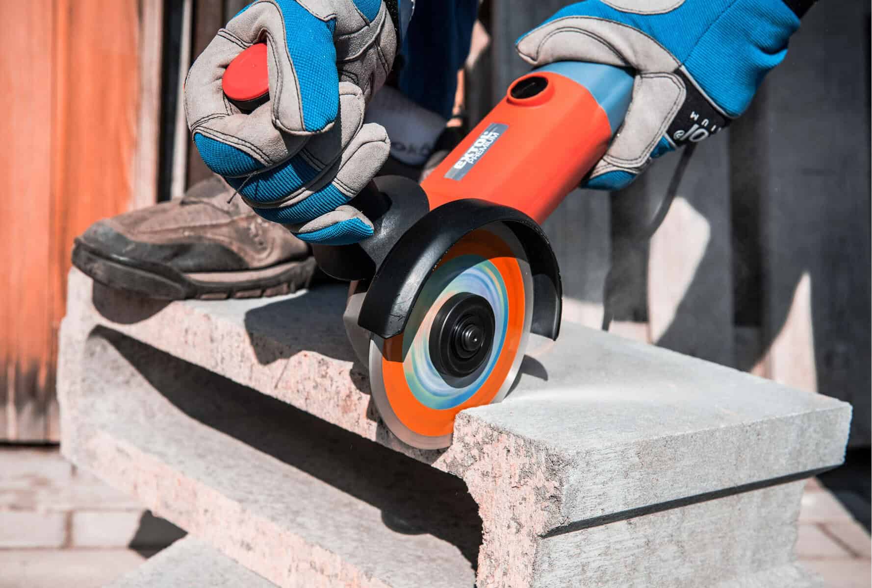 Gloved person uses an angle grinder to cut a concrete block, shaping it as dust rises.