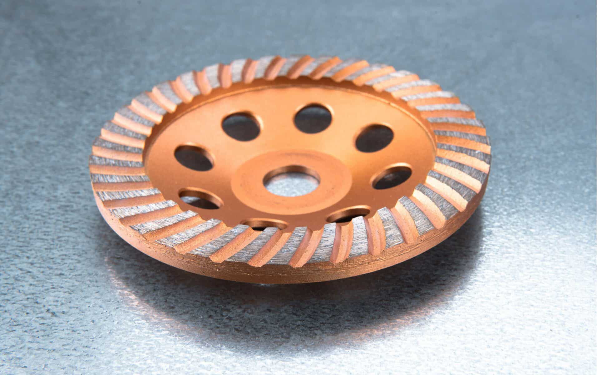 Close-up of an orange grinding wheel with grooves and holes, resting on a metallic surface.