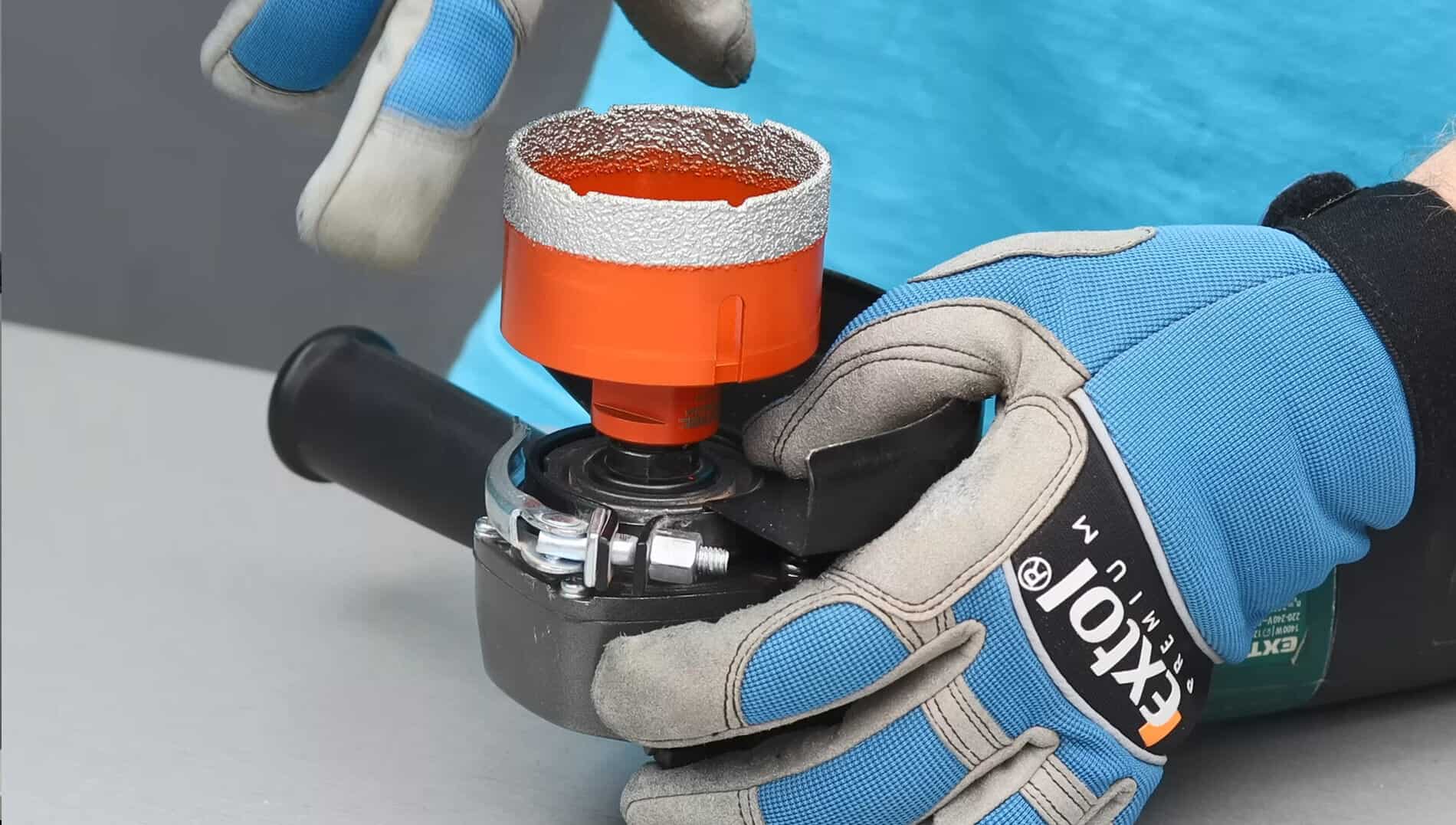 Wearing blue gloves, a person attaches a red diamond hole saw to an angle grinder.