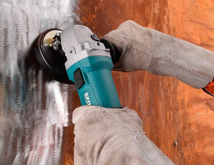 Gloved person uses teal angle grinder, polishing and scratching a metal surface.