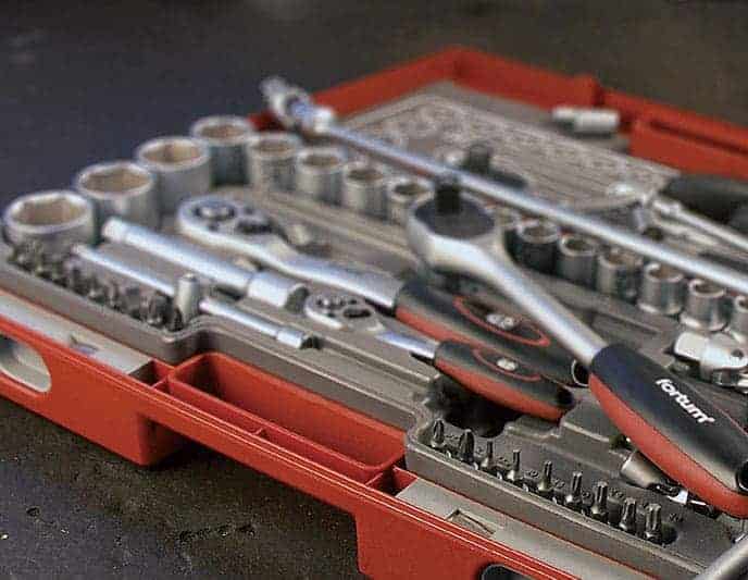 An open red tool case on a table displays neatly organized wrenches, sockets, ratchets, and bits.