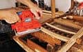 Person using a red electric sander on a wooden chair frame during furniture restoration.