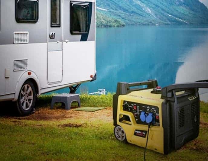 A portable generator sits on grass by a camper near a lake, with mountains in the background.