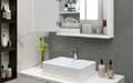 Modern bathroom with white sink, wall cabinets, mirror, toiletries, and a small vase of flowers on the counter.