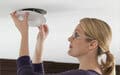 A woman checks or installs a smoke detector on the ceiling.