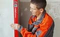 A man in uniform uses a red spirit level to check the alignment of an indoor white wall.