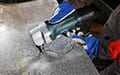 Wearing gloves, a person uses a handheld power tool to cut a sheet of metal.