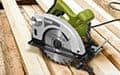 A green and silver electric circular saw on unfinished wooden planks, ready to cut.