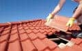 Person in yellow gloves installs a red roof tile on a tiled rooftop under a clear blue sky.