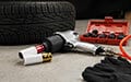 A pneumatic impact wrench, air hose, sockets, gloves, and tire rest on a concrete garage floor.