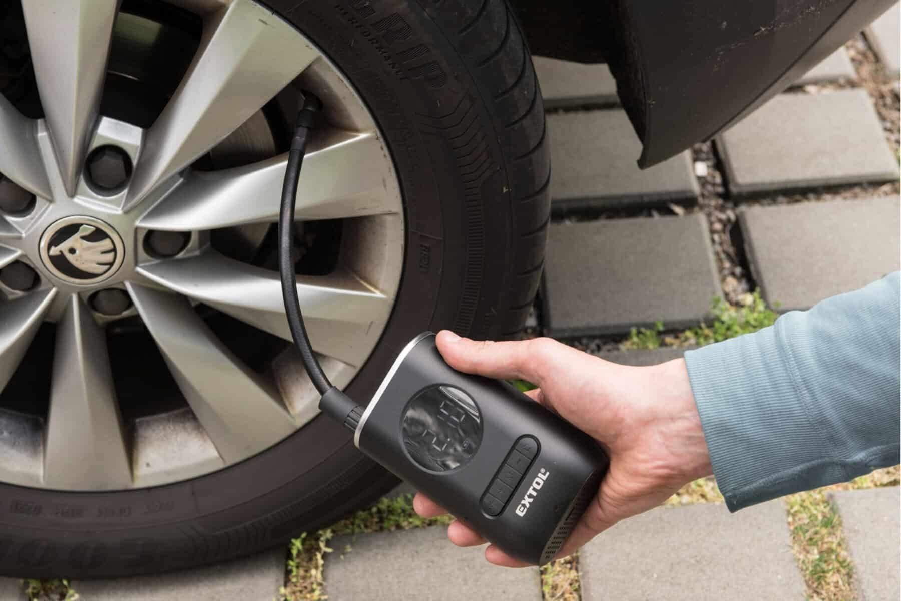 A person inflates a car tire with a portable air compressor, its hose connected to the tire valve.
