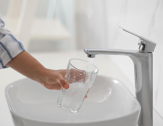 Someone fills a clear glass with water from a modern faucet over a white sink.