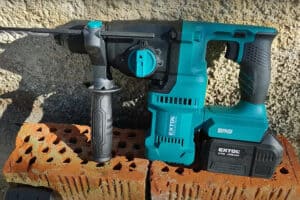 Cordless Extol rotary hammer drill with battery on perforated red bricks, set against a stone wall.