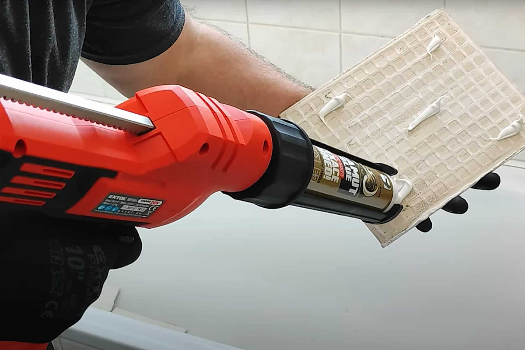 Someone uses a red electric caulking gun to apply adhesive to the back of a plastic panel.