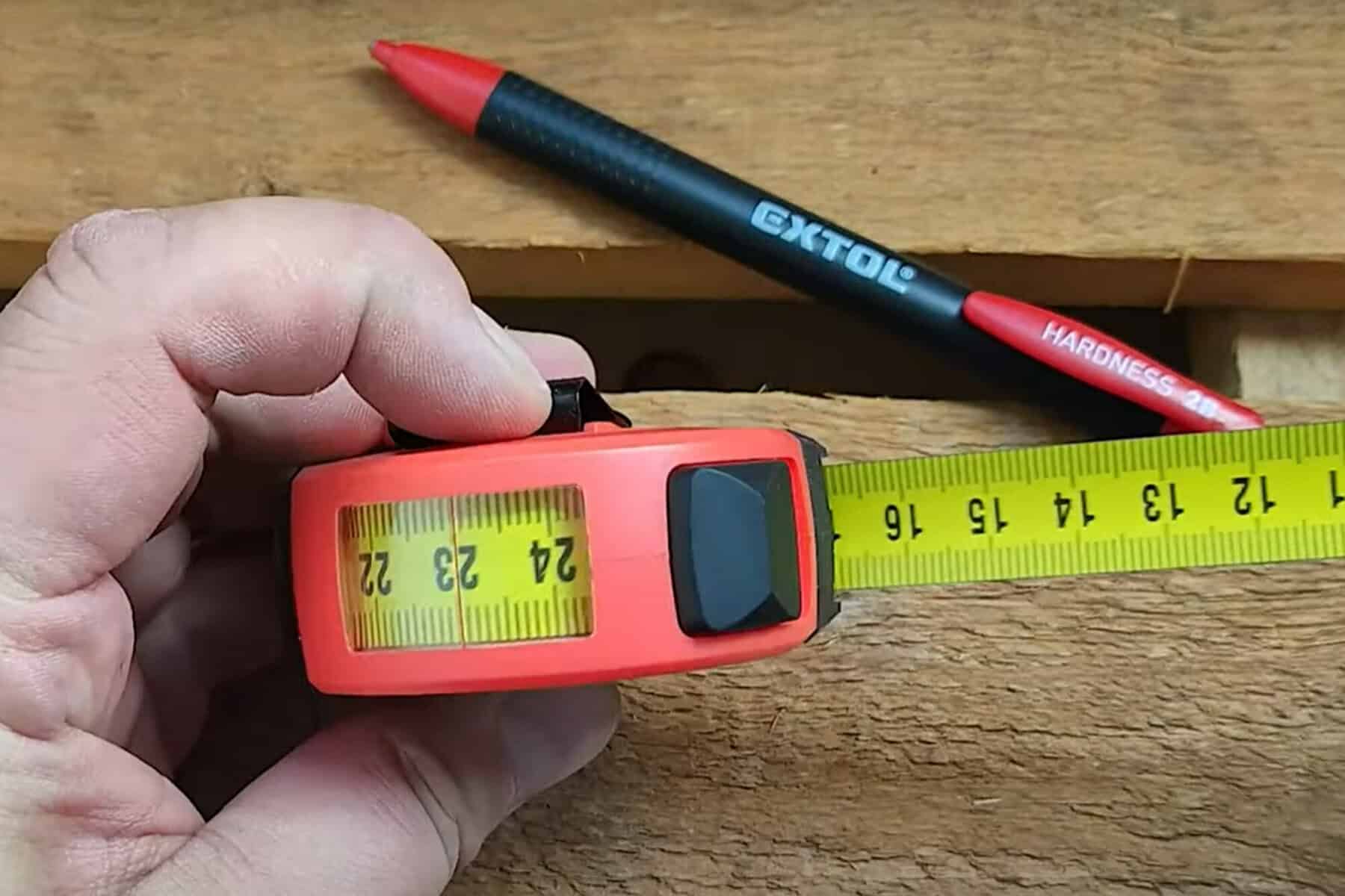 Hand holding tape measure at 22 cm; red and black "EXTOL" pen on wooden surface in background.