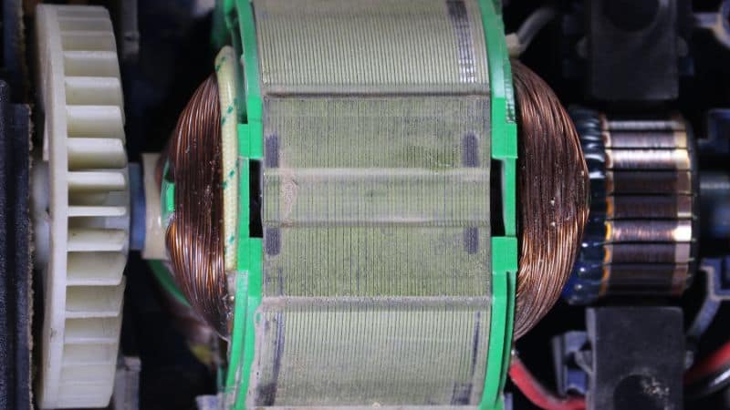 Close-up of an electric motor rotor with copper windings, plastic gears, and electrical components visible nearby.