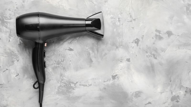 A black hair dryer with a concentrator nozzle rests on a gray textured surface.