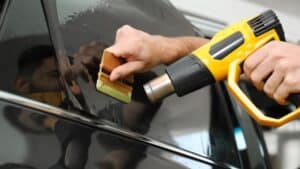 Someone tints a car window using a heat gun and squeegee.